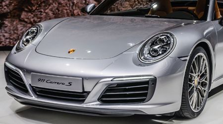 A silver porsche 911 carrera s is parked on a showroom floor.