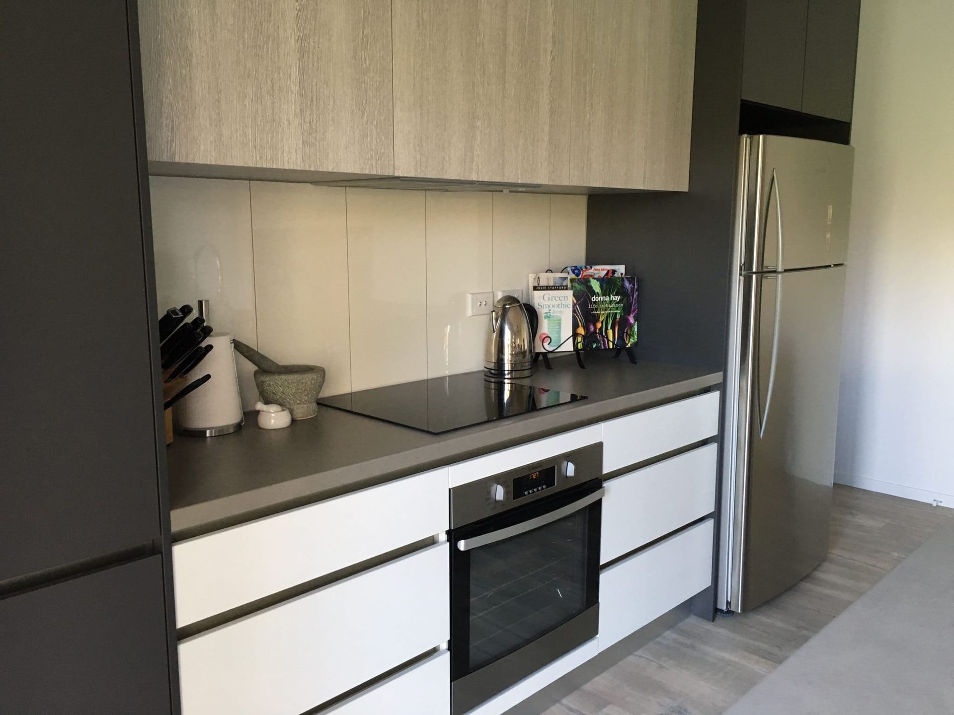Modern kitchen with white and gray cabinets, stainless steel refrigerator, and built-in oven. — Akyrah Kitchens in Gympie, QLD