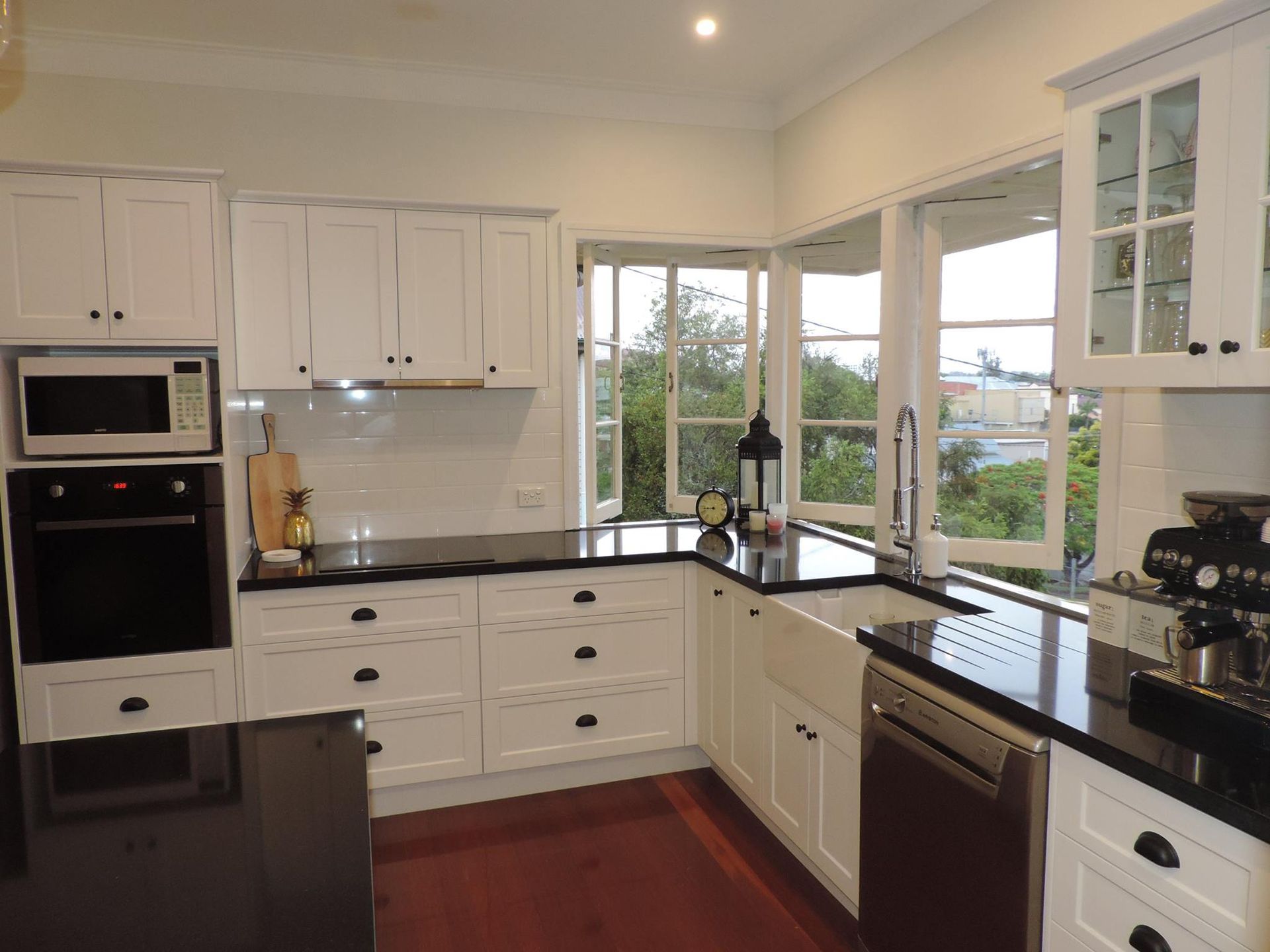 White kitchen with black countertops, cabinets, appliances, and open windows offering a view. — Akyrah Kitchens in Gympie, QLD