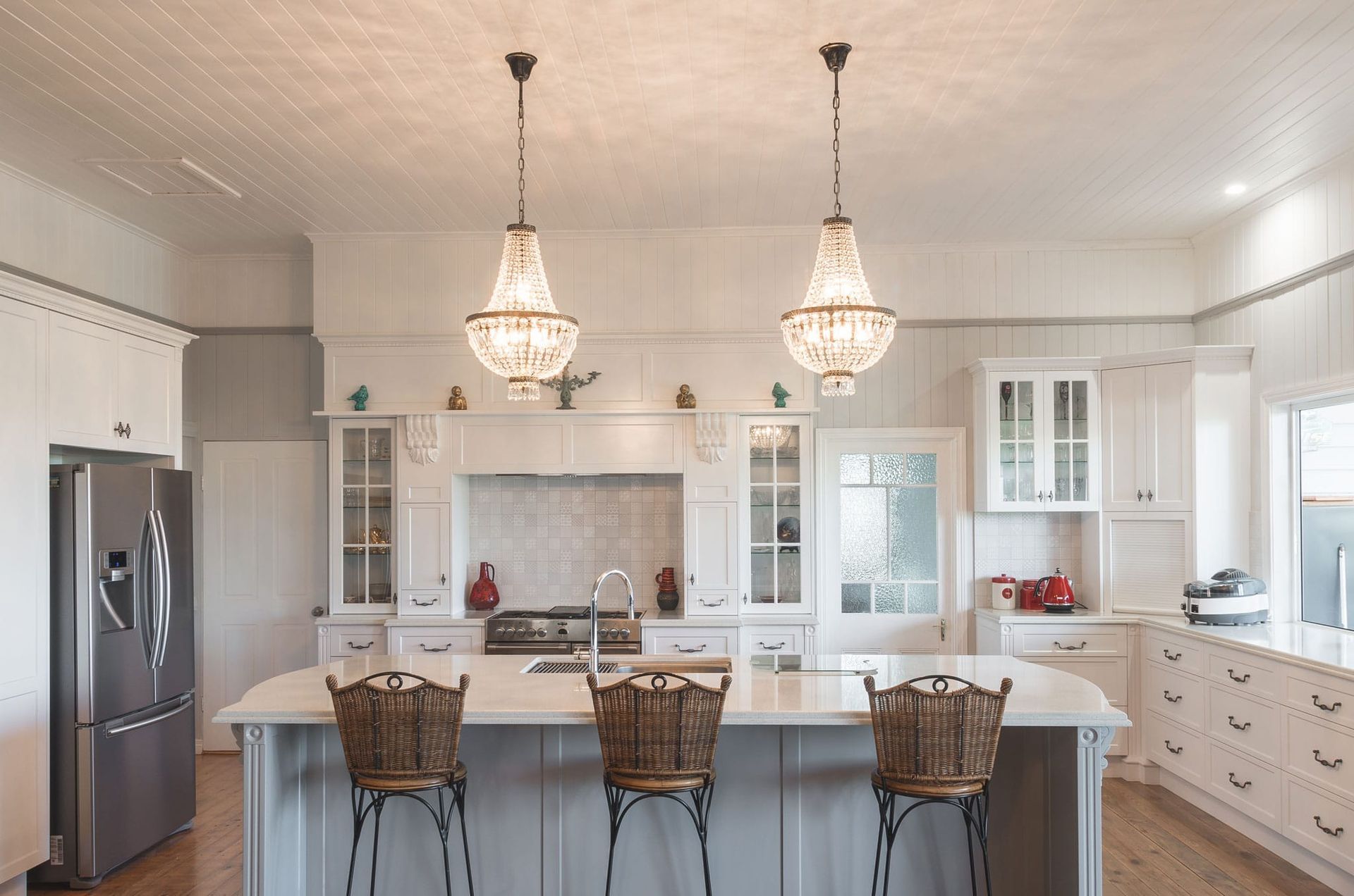 Kitchen With Island, Two Chandeliers, Steel Refrigerator, and Three Woven Bar Stools — Akyrah Kitchens in Gympie, QLD
