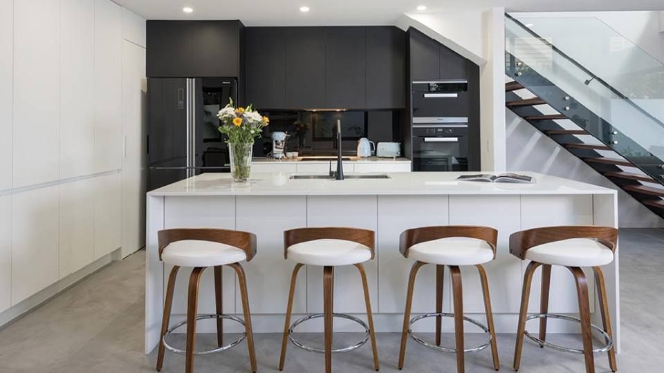 Modern Kitchen With White Island, Black Cabinets, Wood and White Bar Stools, and Staircase — Akyrah Kitchens in Gympie, QLD