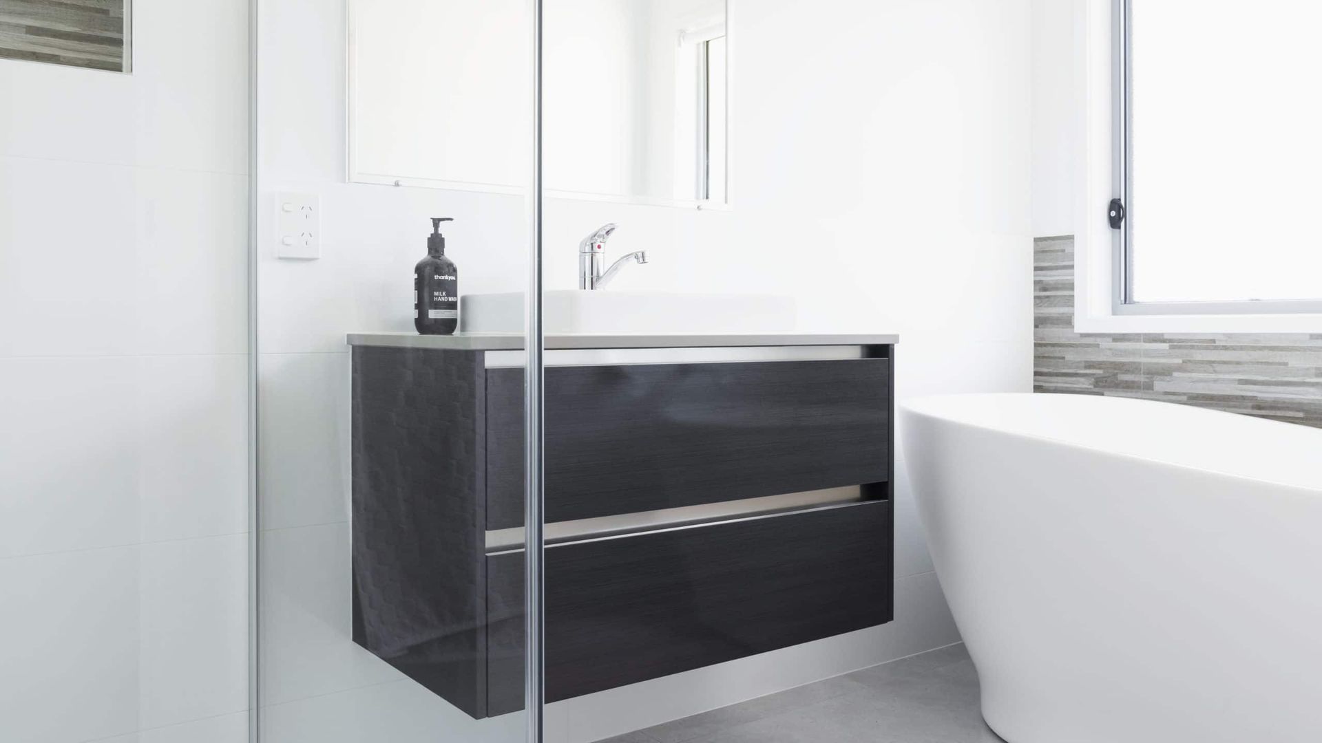 Modern Bathroom With Floating Gray Vanity, White Tub, and Window — Akyrah Kitchens in Gympie, QLD