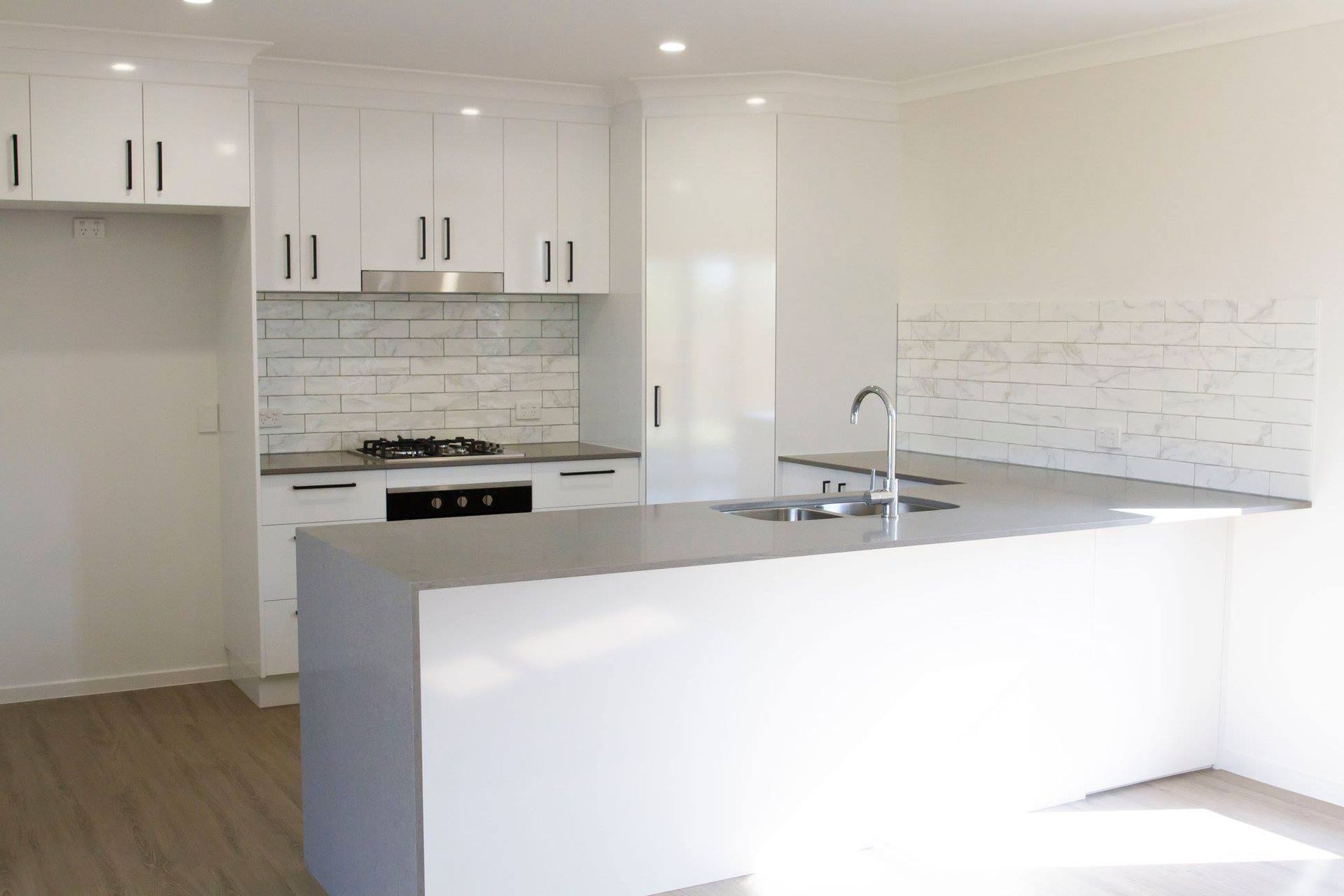 White Kitchen With Island, Cabinets, Brick-style Backsplash, and Stainless Steel Appliances — Akyrah Kitchens in Gympie, QLD