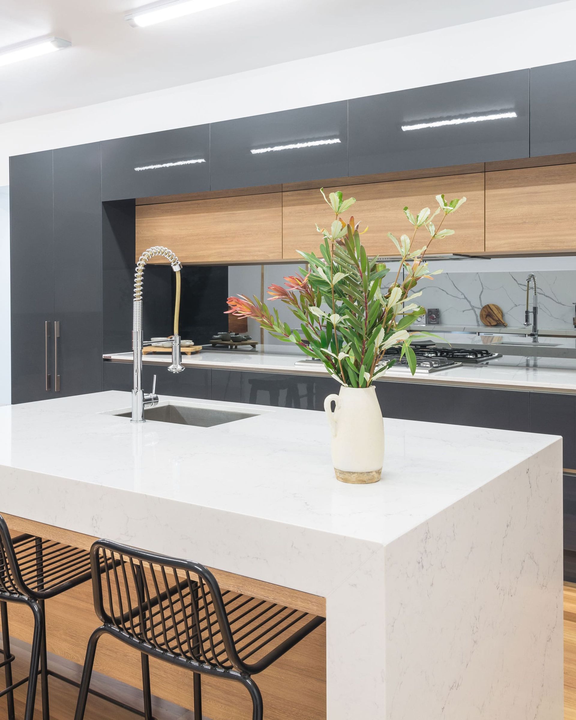 Modern Kitchen With White Island, Black Bar Stools, Wooden Cabinets, and a Vase of Flowers — Akyrah Kitchens in Gympie, QLD