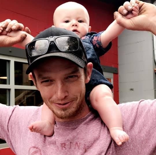 A man wearing sunglasses is carrying a baby on his shoulders