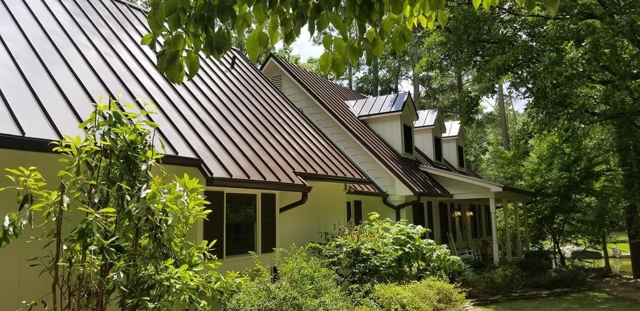 A white house with a brown roof is surrounded by trees and bushes.