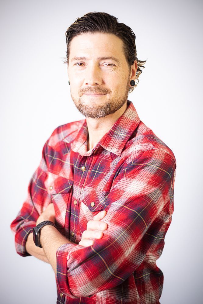 A man in a plaid shirt is standing with his arms crossed.
