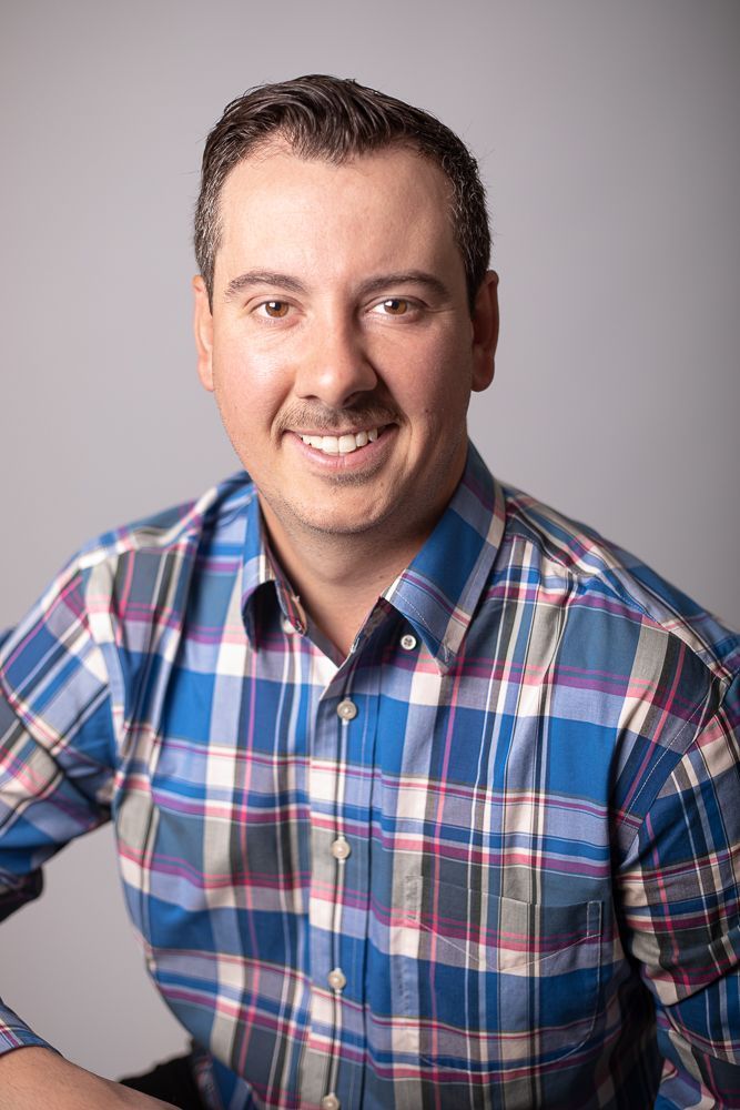 A man in a blue plaid shirt is smiling for the camera.