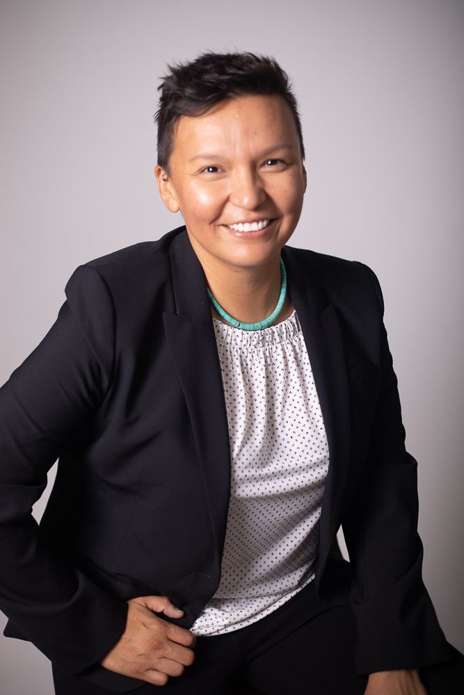 A woman wearing a black jacket and a white shirt is smiling for the camera.
