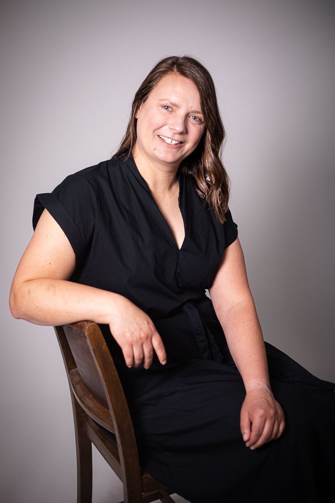 A woman in a black dress is sitting in a chair and smiling.
