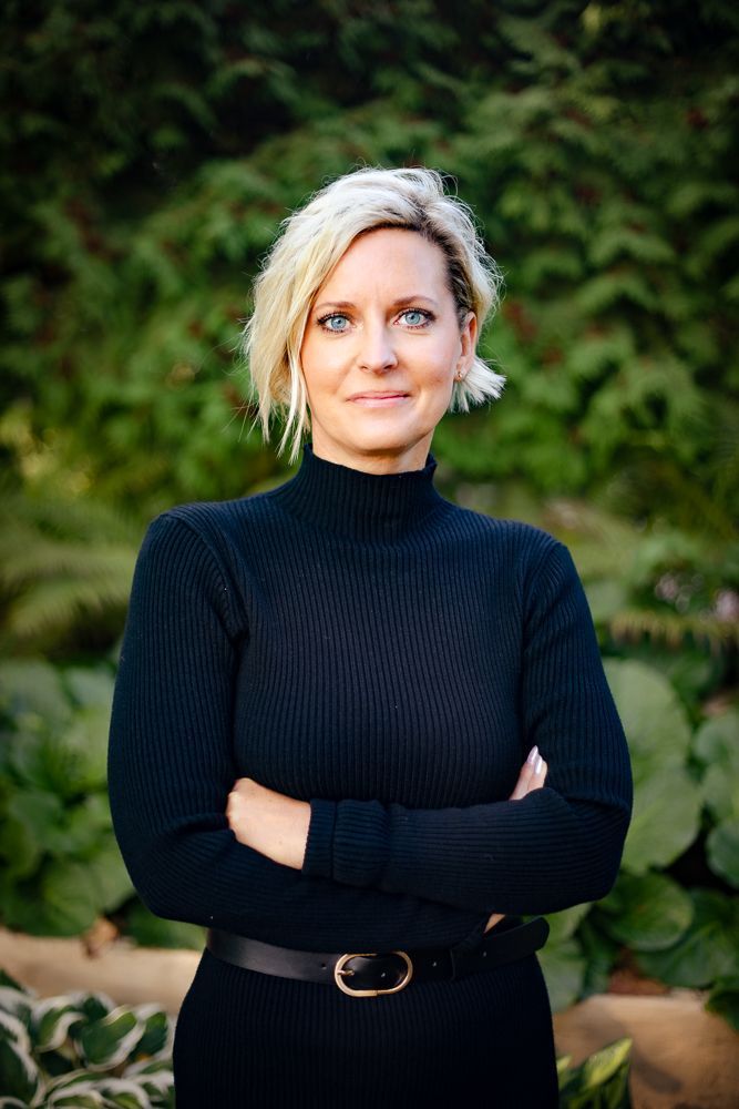 A woman in a black sweater is standing with her arms crossed.