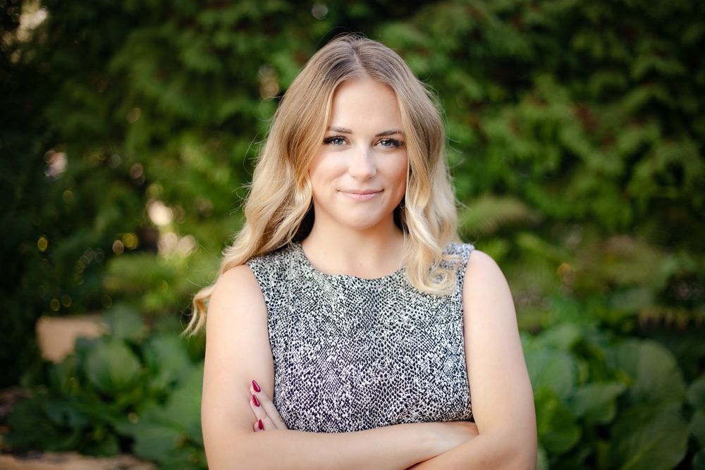 A woman is standing with her arms crossed in front of a green background.
