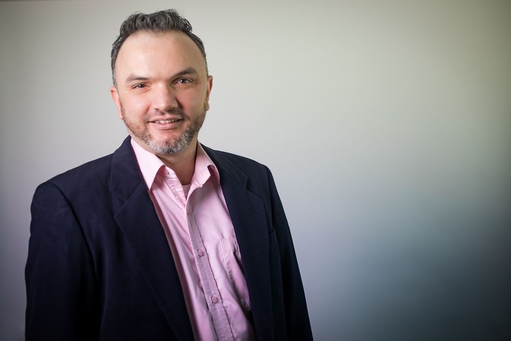 A man with a beard is wearing a suit and a pink shirt.