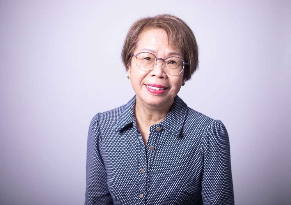 A woman wearing glasses and a blue shirt is smiling for the camera.