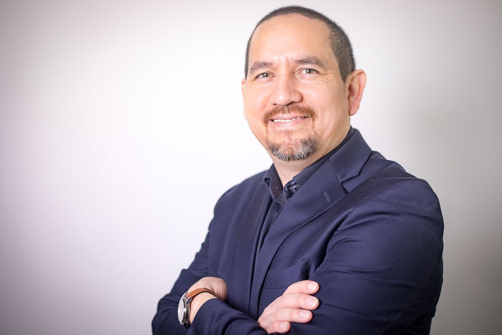 A man in a suit is standing with his arms crossed and smiling.