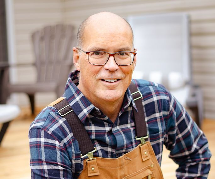 A man wearing overalls and glasses is smiling for the camera.