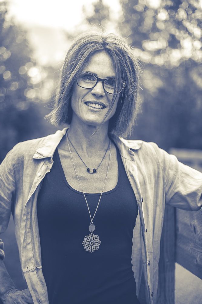 A woman wearing glasses and a necklace is smiling in a black and white photo.