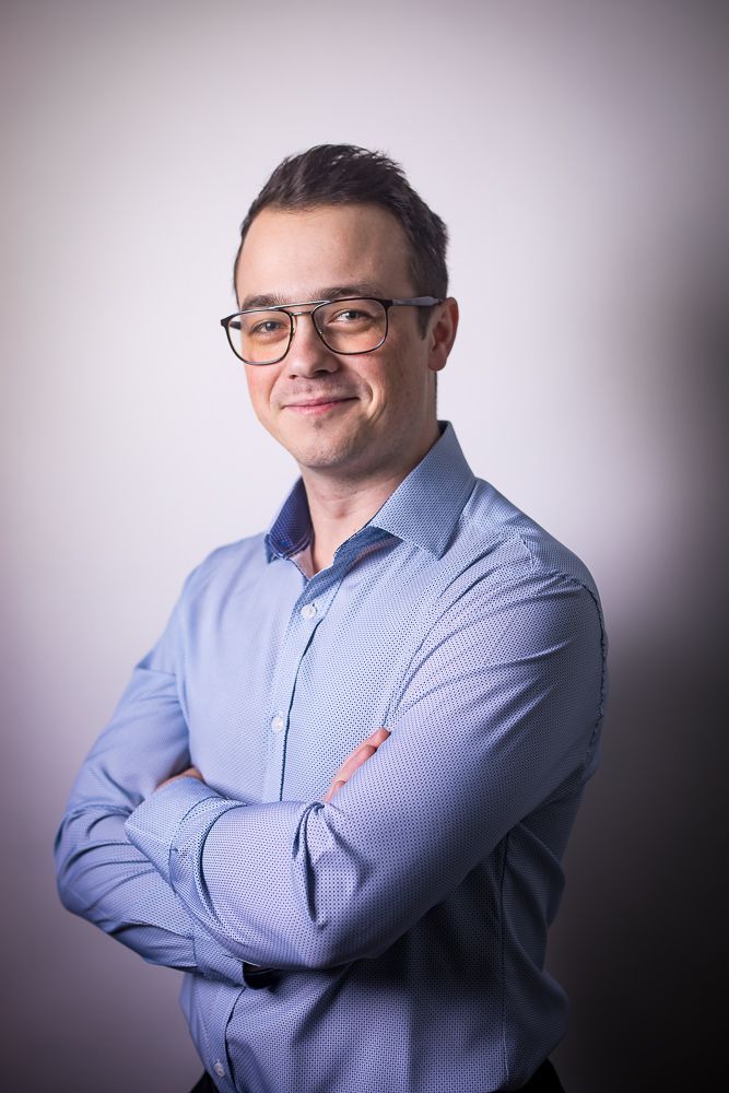 A man wearing glasses and a blue shirt is standing with his arms crossed.