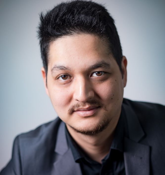 A man in a suit and black shirt is looking at the camera.