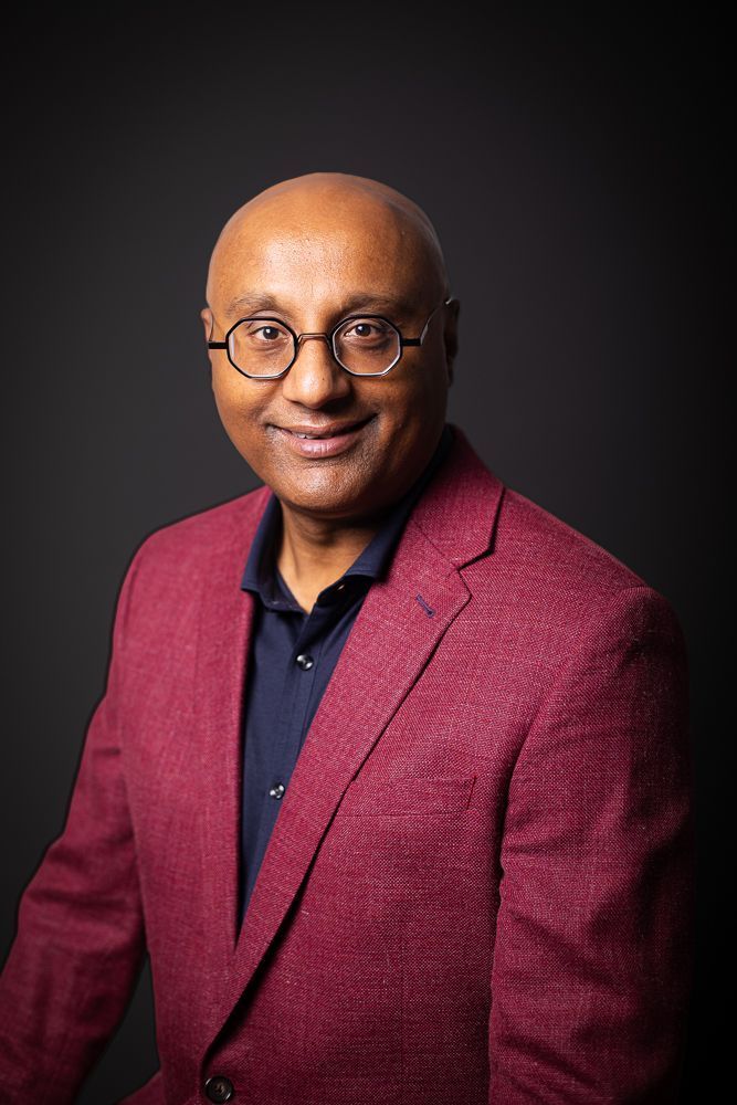A bald man wearing glasses and a red jacket is smiling for the camera.