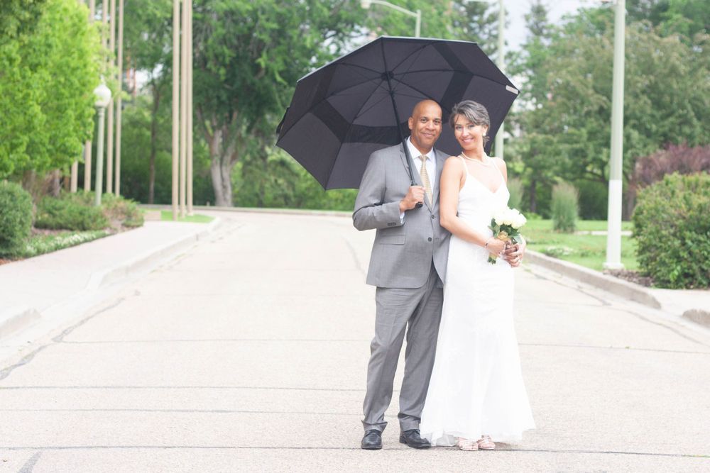 A bride and groom are standing under an umbrella on a street.
