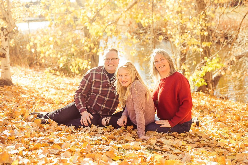 A family is sitting on a pile of leaves in the woods.