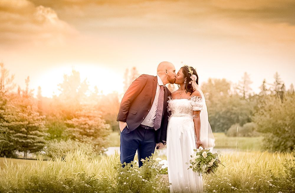 A bride and groom are kissing in a field at their wedding.