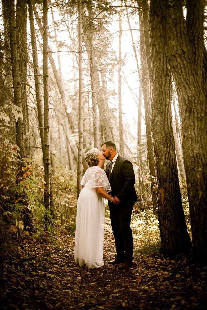 A bride and groom are kissing in the woods.