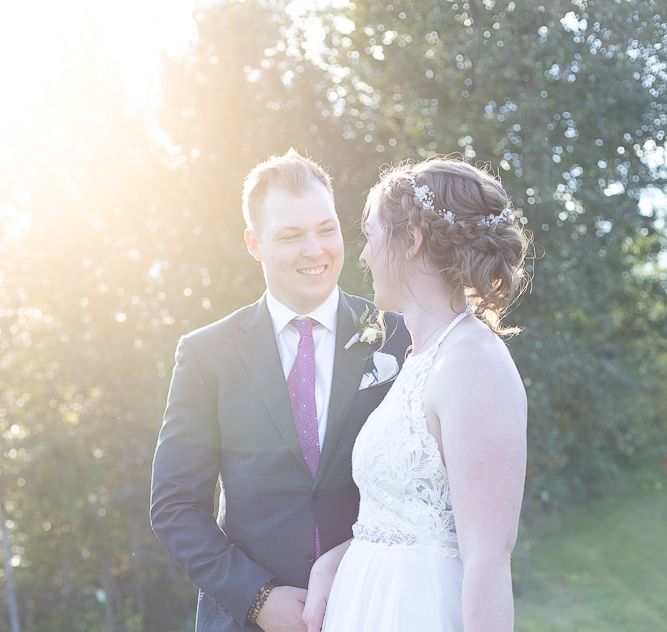 A bride and groom are standing next to each other and smiling at each other.