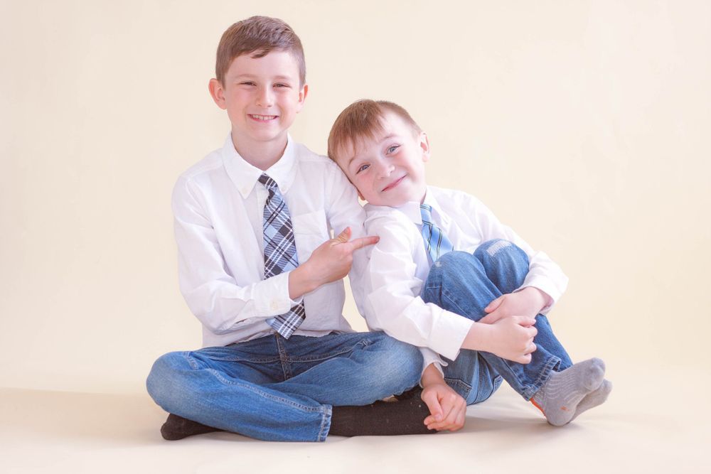 Two young boys are sitting on the floor hugging each other.
