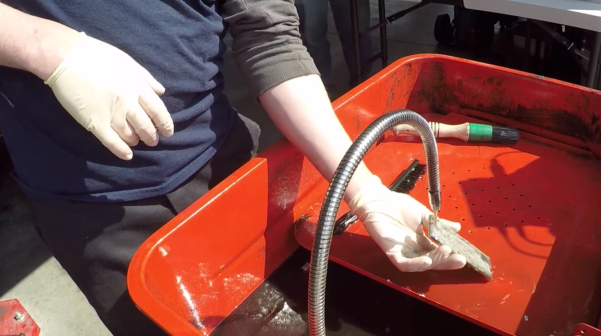 A person wearing gloves is cleaning a hose in a red tray.