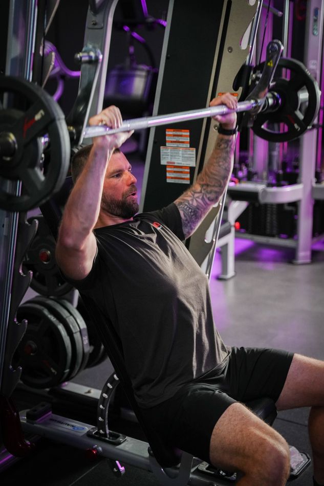Een persoon doet lat pulldowns aan een kabelmachine in een sportschool met paarse verlichting.