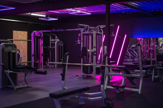 een sportschool vol met veel fitnessapparatuur en paarse lichten.