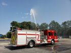 A red and white fire truck is spraying water in a parking lot.