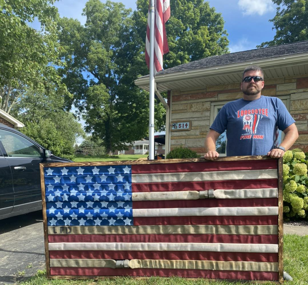 A man is holding an american flag in front of a house.