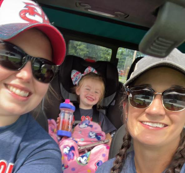 Two women are taking a selfie with a little girl in a car seat