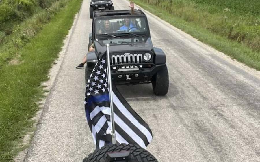 A jeep with an american flag on the back of it is driving down a dirt road.