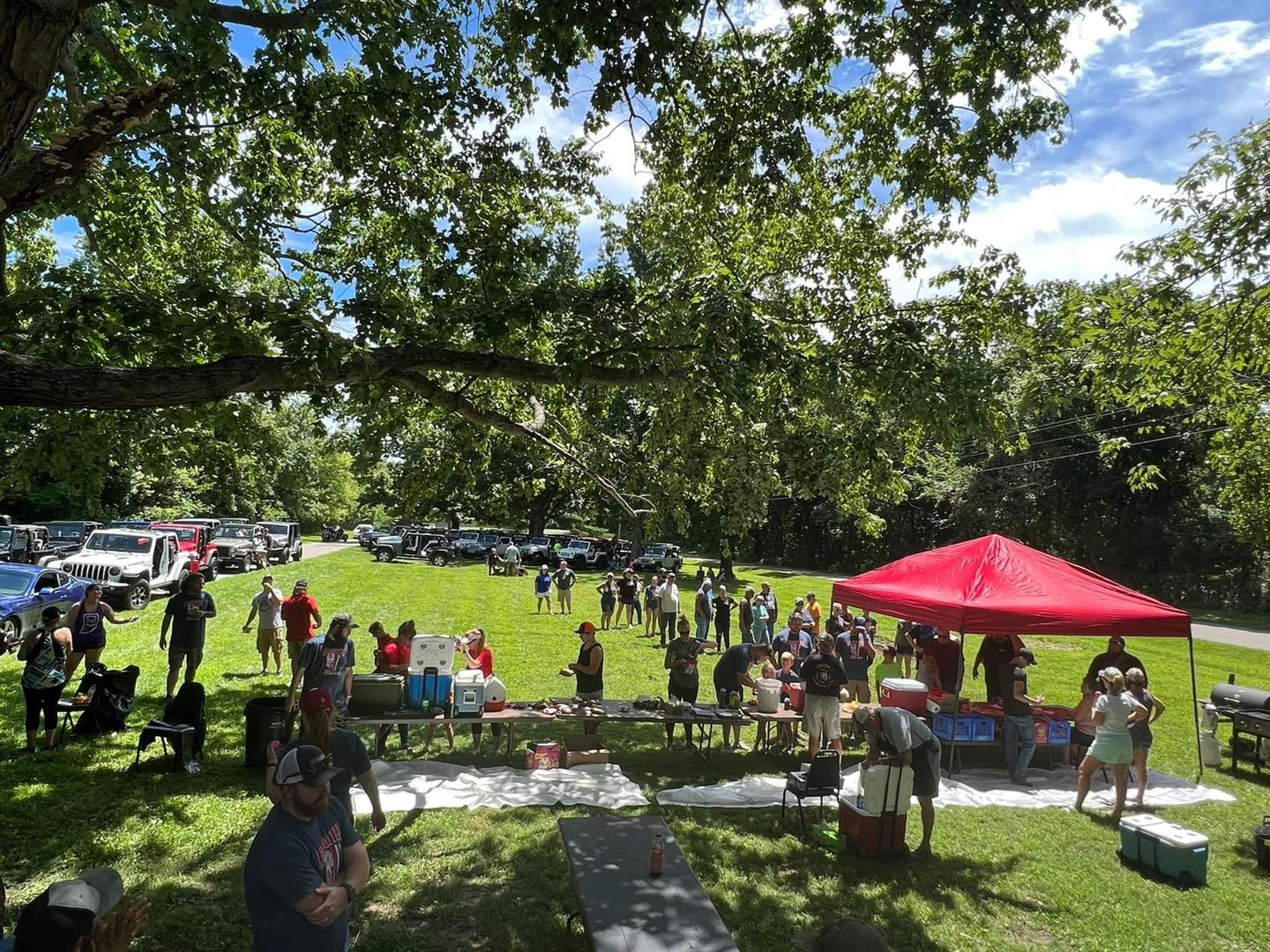 A group of people are sitting under a red tent in a park.