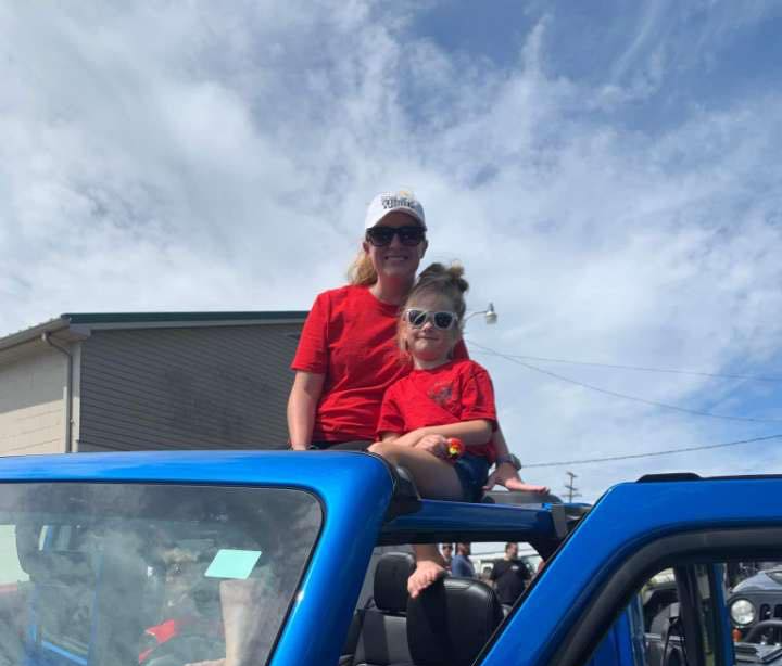 A woman and a child are sitting on the roof of a blue truck.