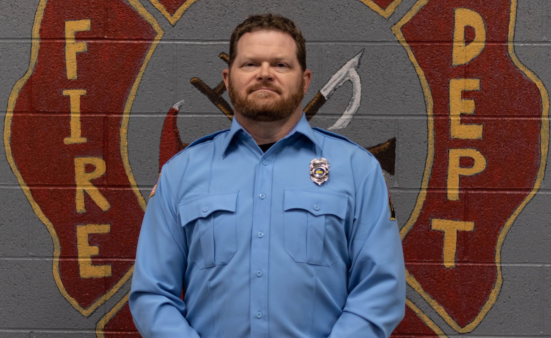 A man in a blue shirt is standing in front of a fire department logo.