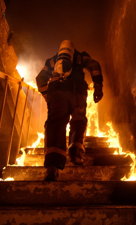 A fireman is walking up a set of stairs in front of a fire.