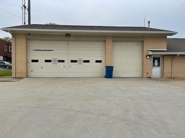 A brick building with a white garage door and a blue trash can in front of it.