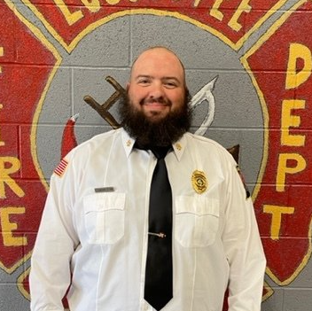 A man with a beard is wearing a white shirt and black tie.
