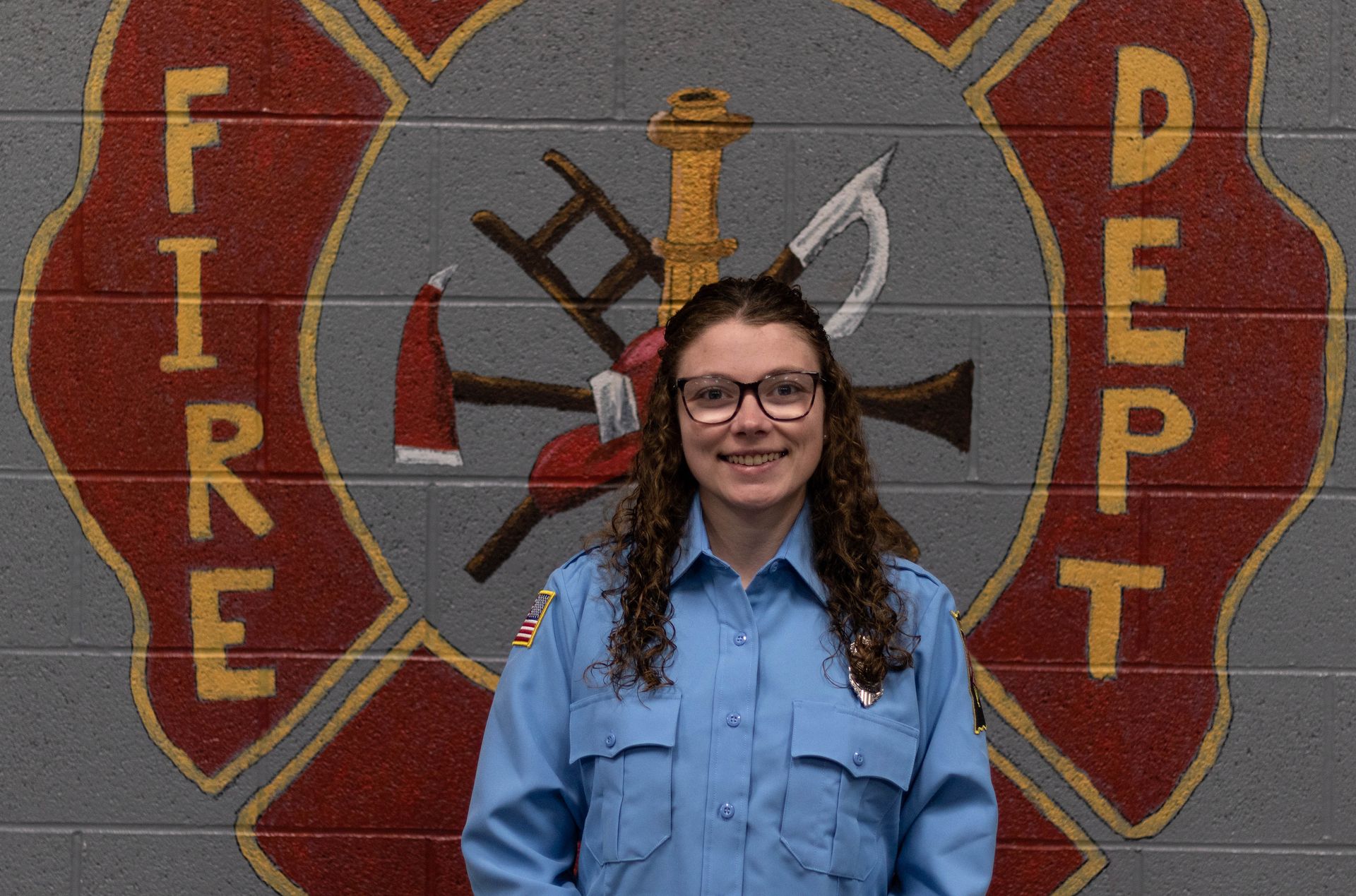 A woman in a blue uniform is standing in front of a fire department logo.