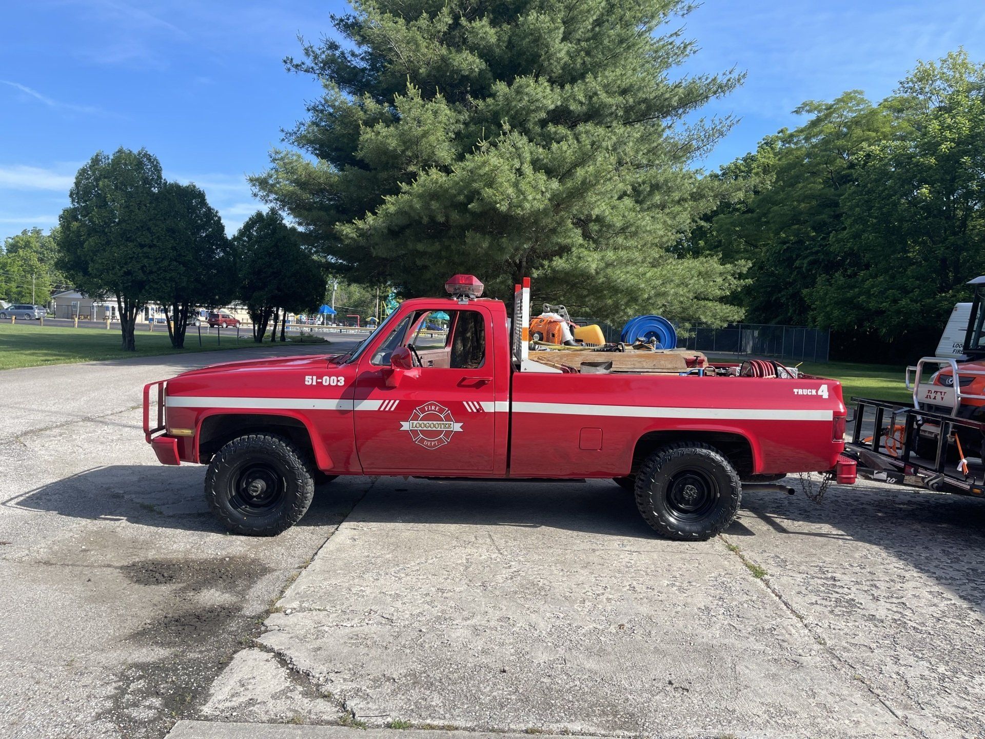 A red truck is parked in a parking lot next to a tree.