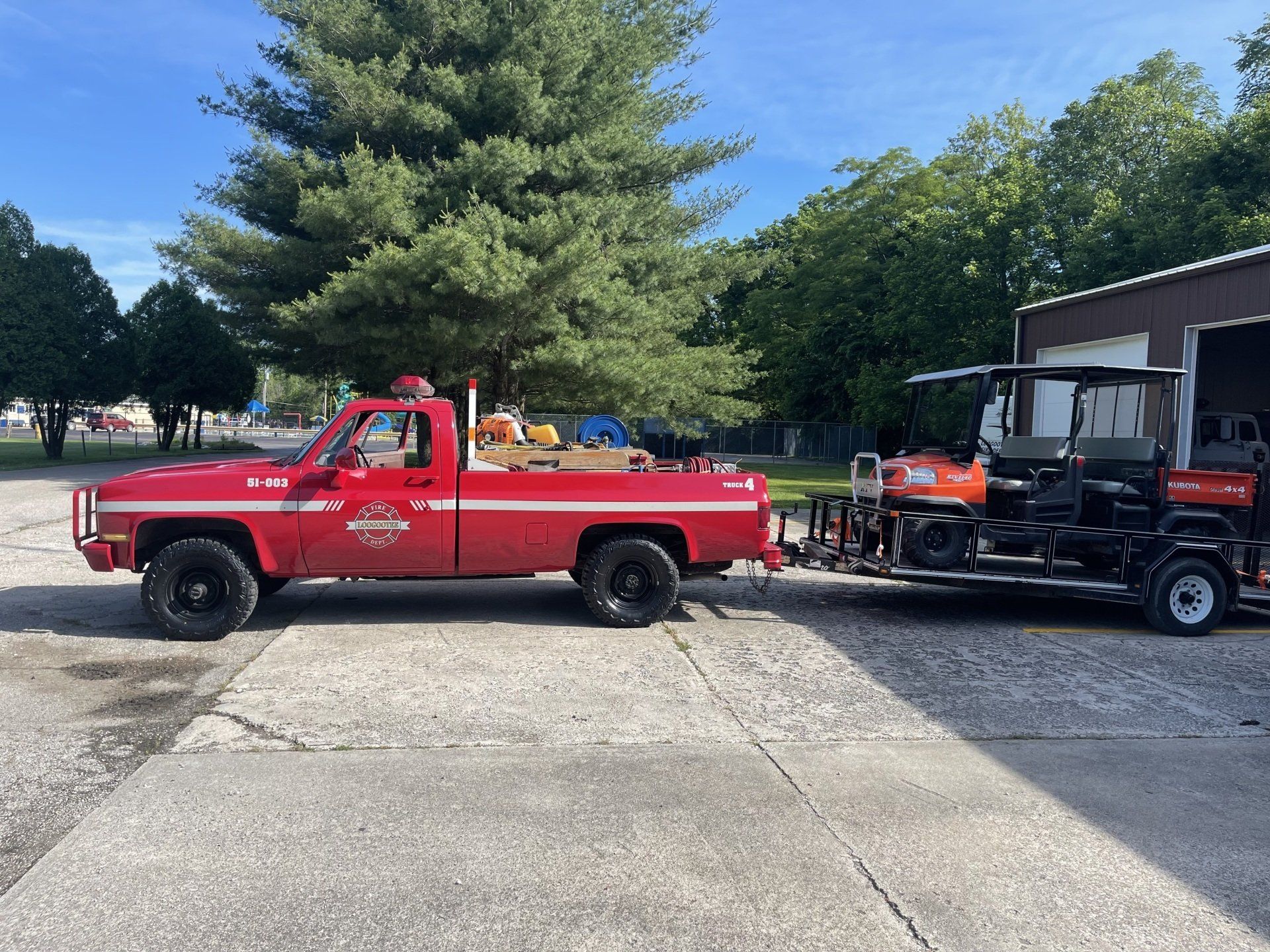 A red truck is pulling a golf cart on a trailer.