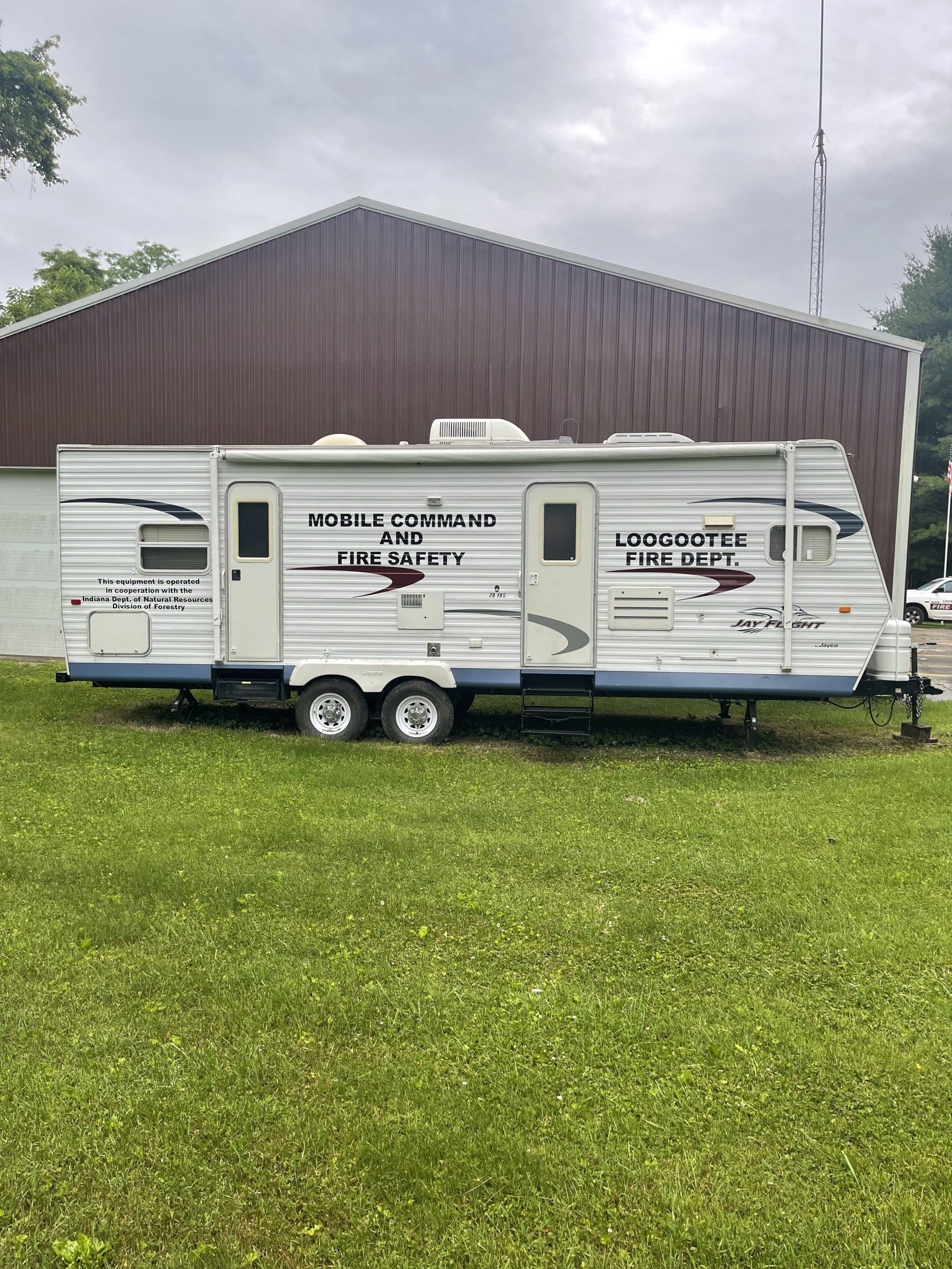 A white trailer is parked in a grassy field in front of a building.