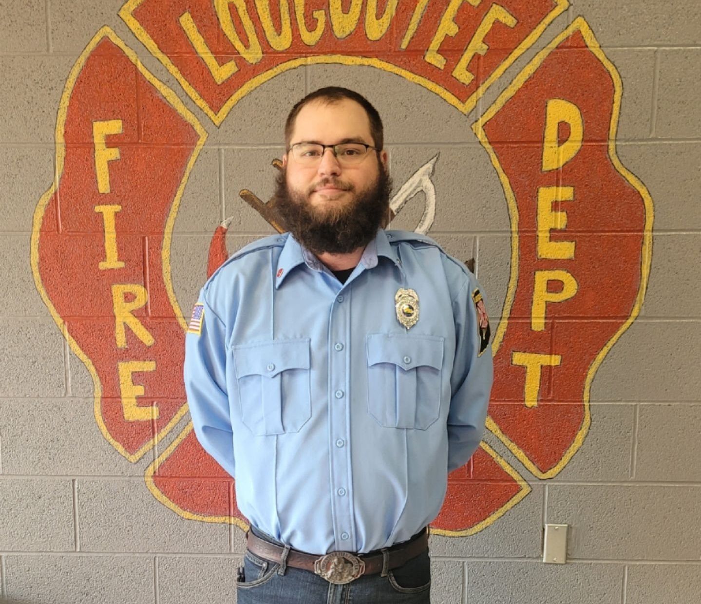 A man with a beard is standing in front of a fire department logo