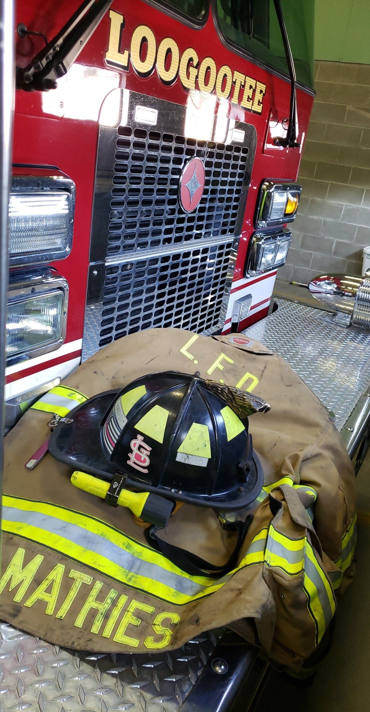 A fireman 's helmet and gloves are sitting on the hood of a fire truck.