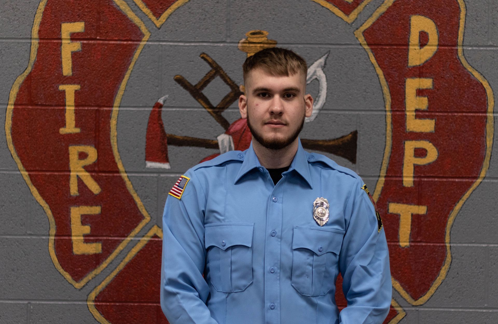 A man in a blue shirt is standing in front of a fire department logo.